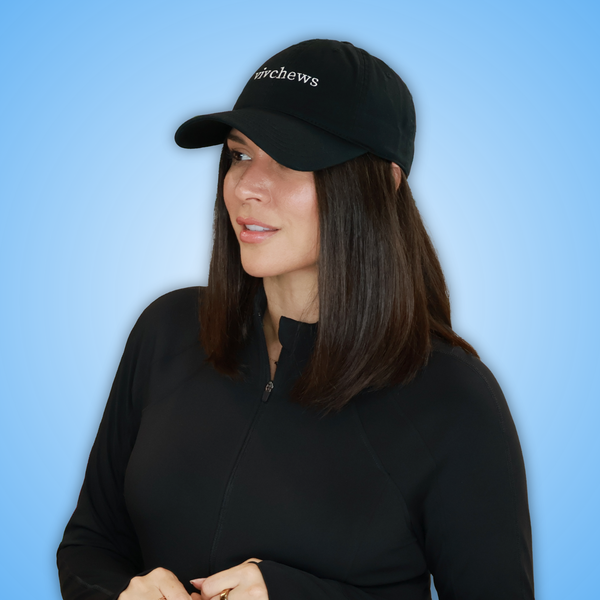 Vivian wearing a black baseball cap with the brand name 'vivchews' embroidered in white on the front, paired with a black zip-up long-sleeve shirt, set against a solid light blue background.
