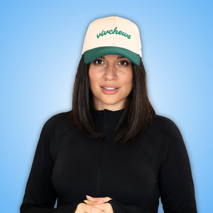 Vivian with shoulder-length dark brown hair is shown from the chest up, wearing a cream and green trucker hat with the word 'vivchews' embroidered in green on the front, against a light blue gradient background.