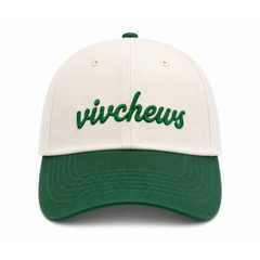 A baseball cap with an off-white crown and a dark green curved brim, featuring the word 'vivchews' embroidered in green script across the front.