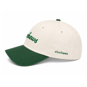 An off-white baseball cap with a dark green visor and green embroidered details, including the word 'chews' on the front and 'vivchews' on the side.